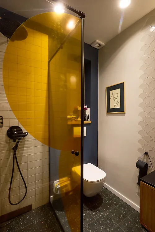 A bathroom with a bold curved yellow panel, white tiles and a framed print