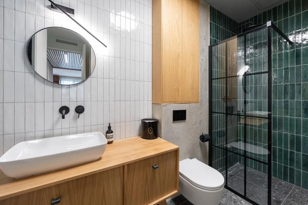 Bathroom with oak vanity, white wall tile and a black framed shower in deep green tile