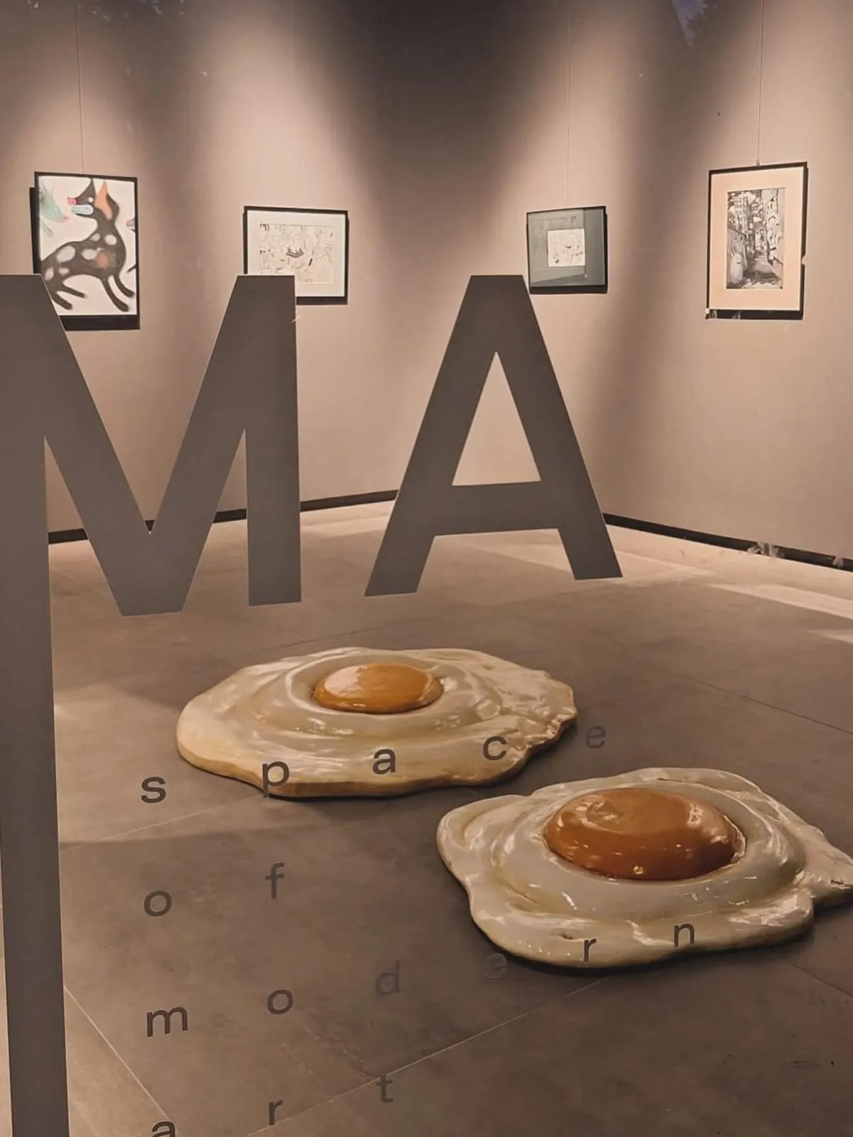 Ceramic fried eggs on the gallery floor in front of the SOMA lettering and framed drawings
