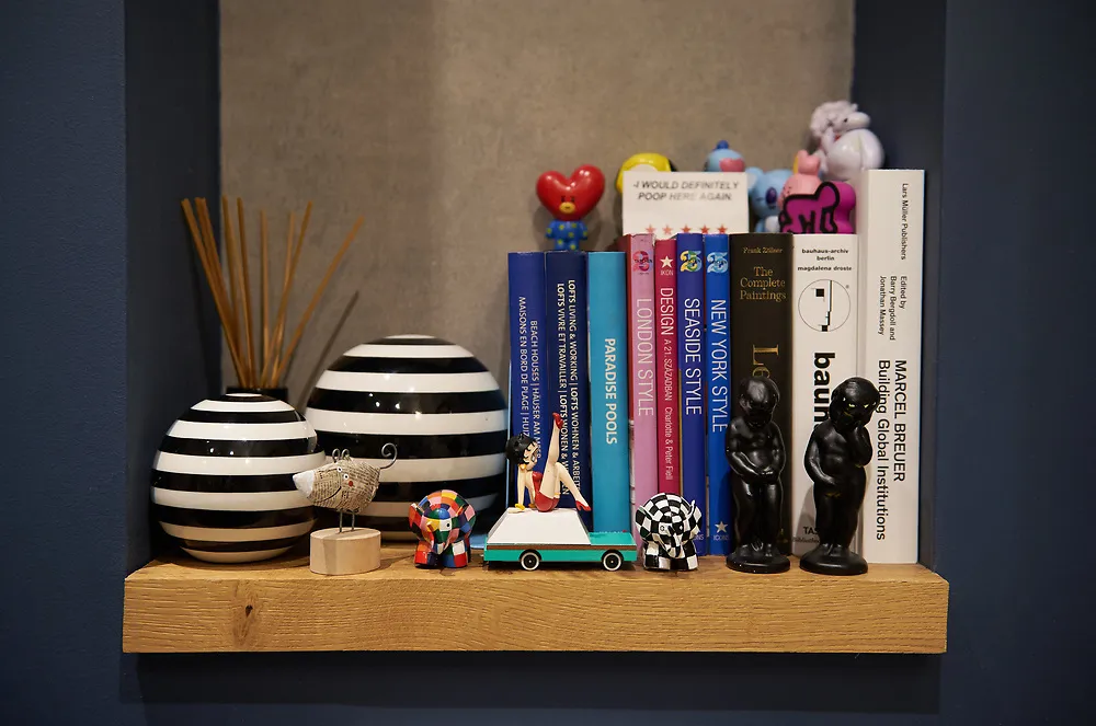 A floating oak shelf on a navy wall with striped ceramic vases, books and small figures