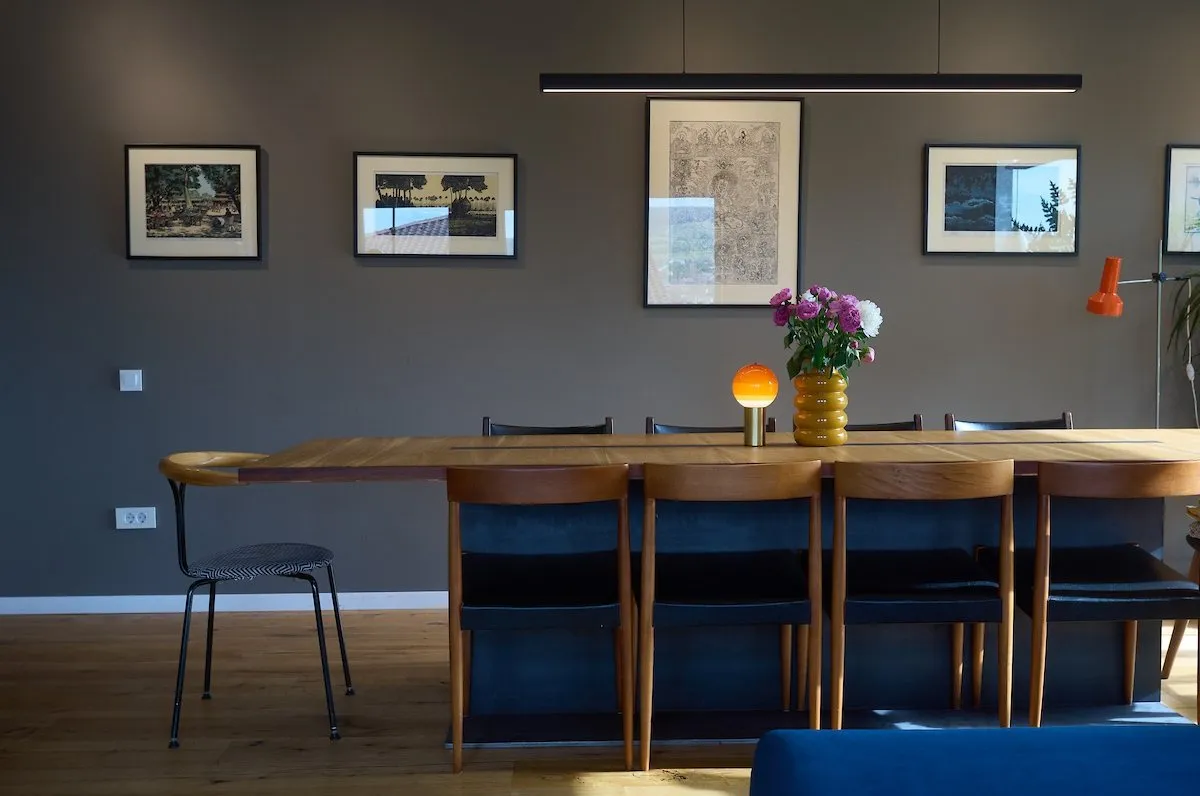 Long oak dining table with teak chairs and framed prints on a grey wall