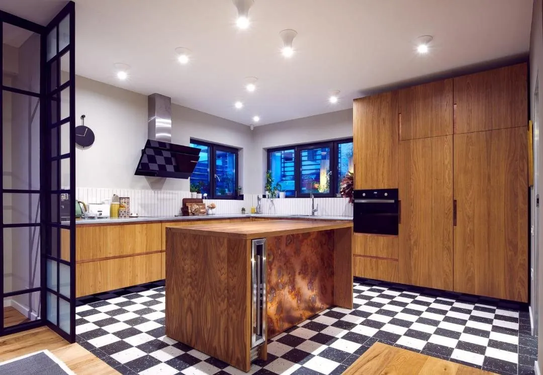 Oak kitchen island with a patinated copper panel on a black and white terrazzo check floor