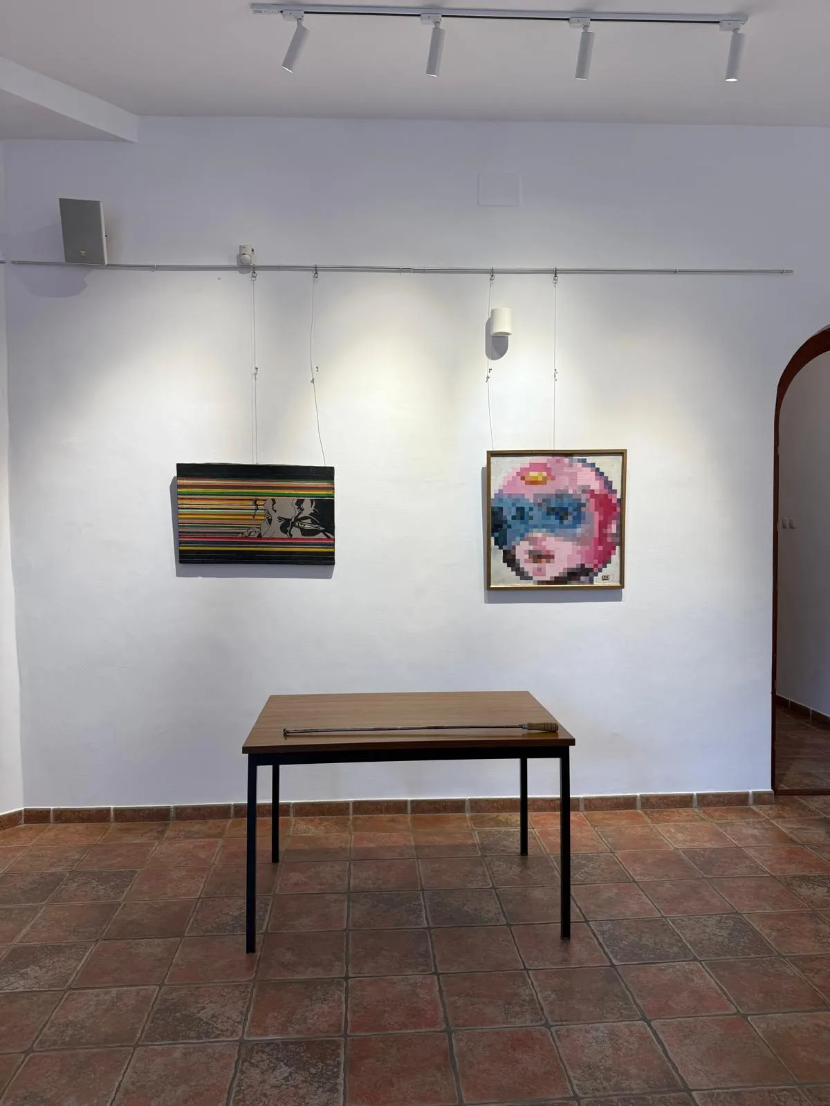 A striped panel and a pixel portrait above a small table on a tiled floor