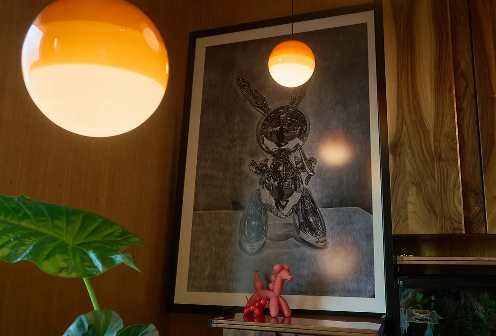 Two orange glass globe lamps glowing in front of a large framed print and a monstera leaf