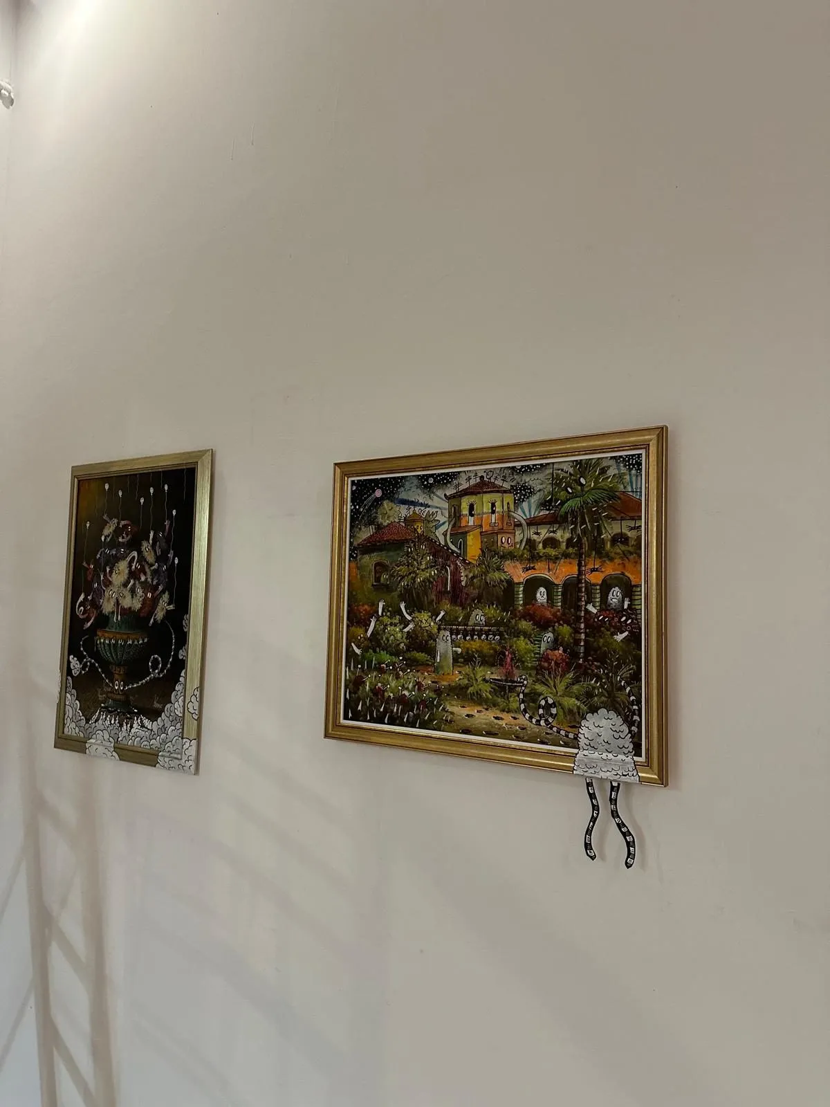 Two repainted classics in gilt frames seen at an angle on a white wall