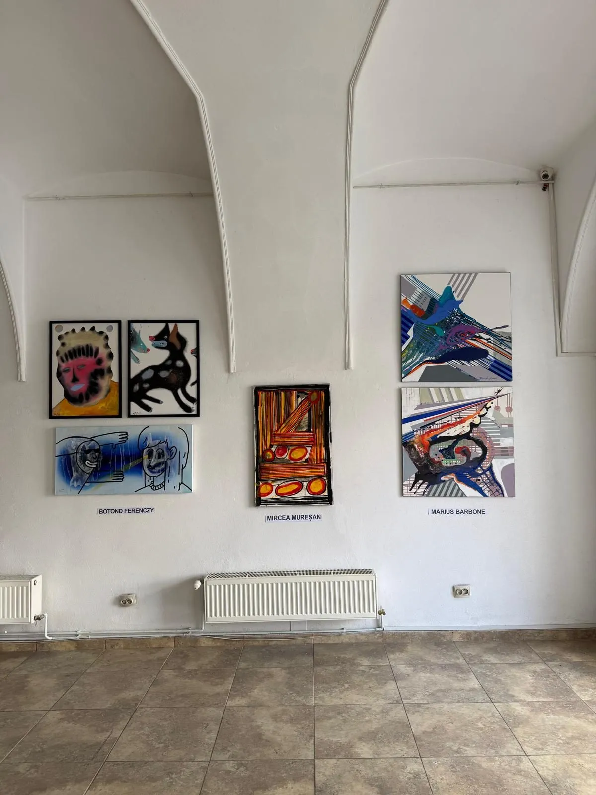A vaulted white gallery with works by three artists on the walls