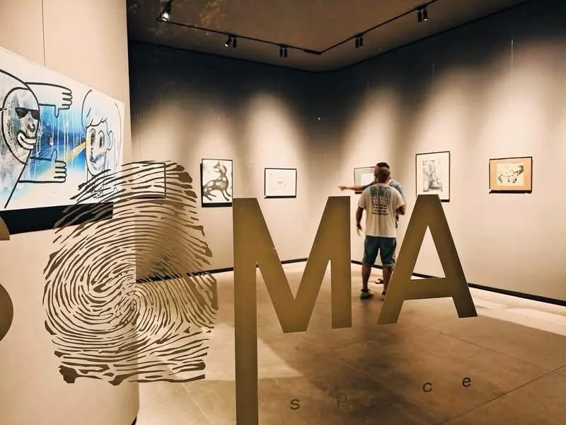 A visitor looking at drawings beyond a large painted fingerprint and the SOMA letters